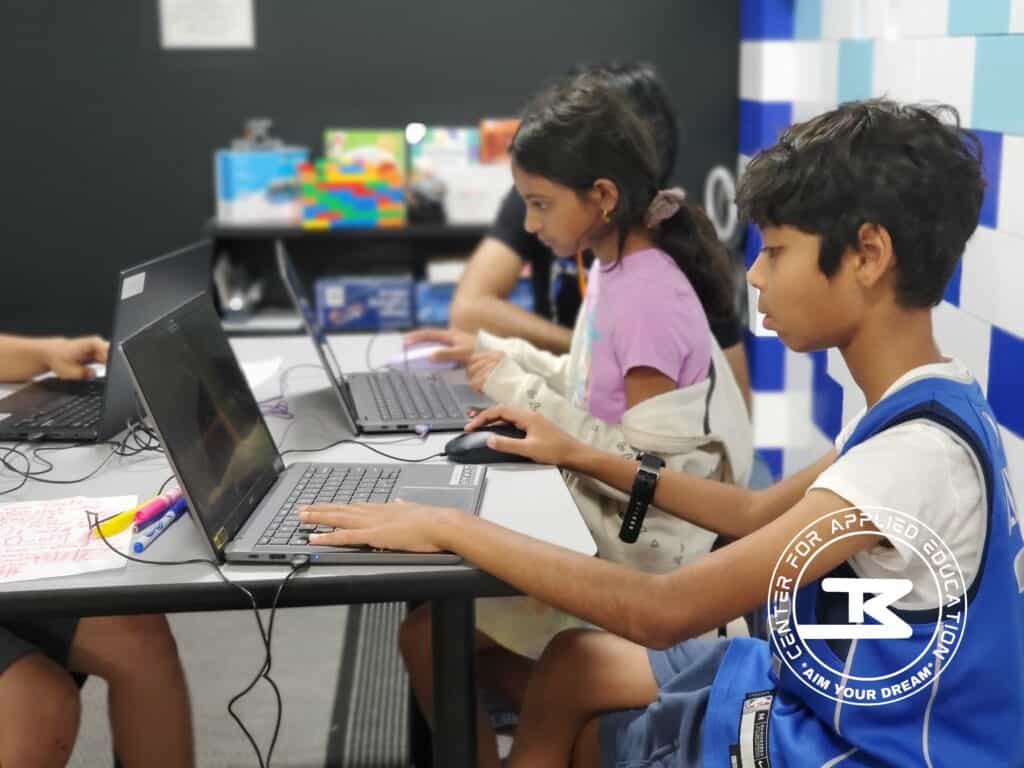 Laptops and children working on computers, coding, and learning technology skills in a classroom setting.