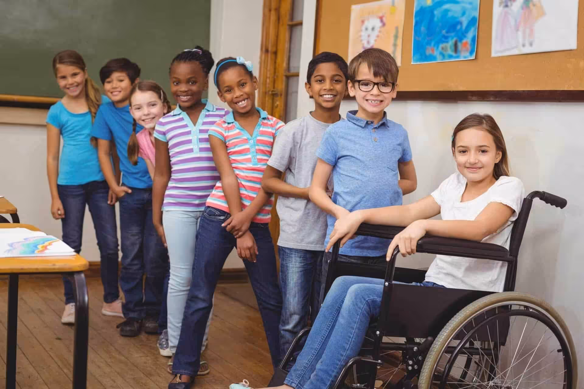 Diverse group of smiling children in a classroom, fostering inclusion and teamwork for kids with disabilities.