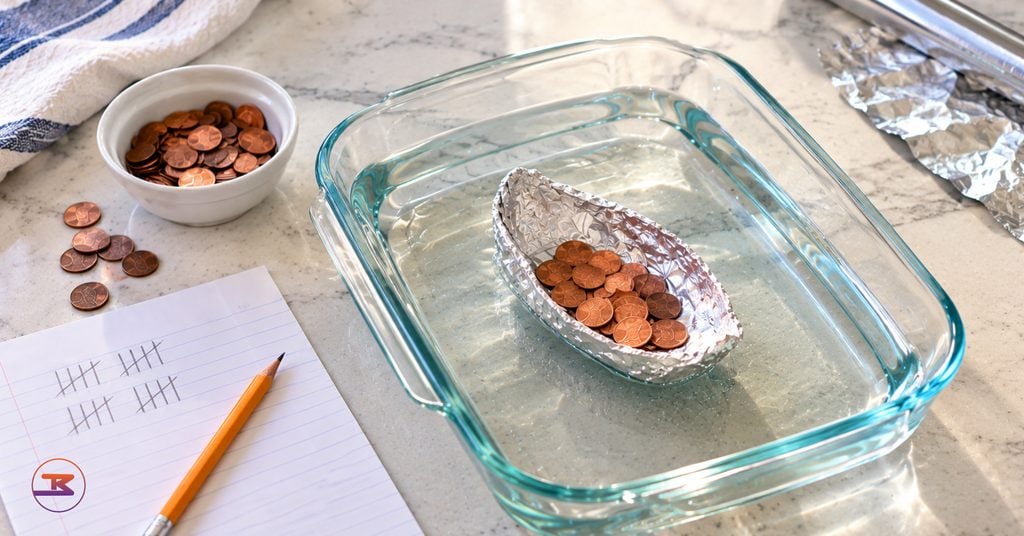 Foil boat holding a pile of pennies in a baking dish of water